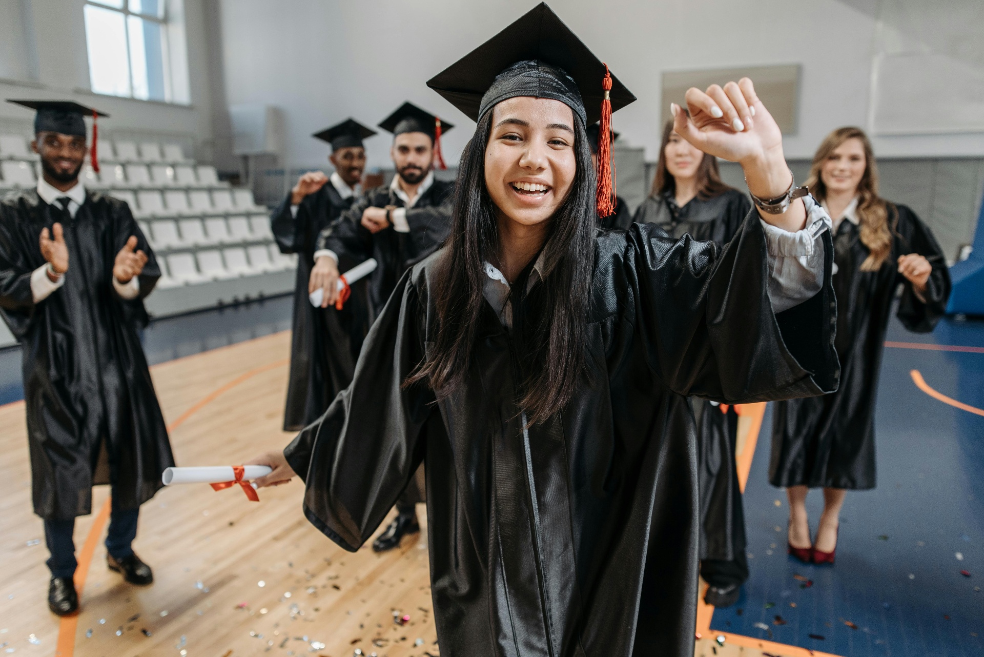 A joyful young graduate in cap and gown celebrating with peers at commencement