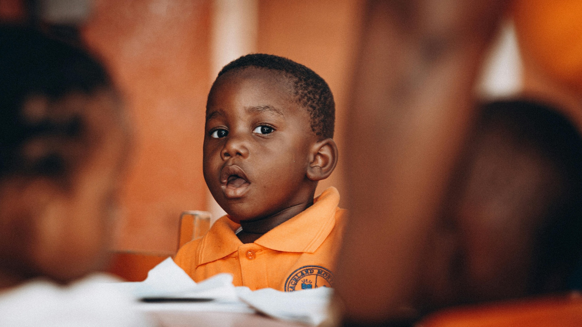 A young child in an orange shirt attentively engaged in an early learning setting